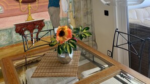 Una habitació amb un mural de paret de marbre, una taula de vidre amb un arranjament floral al centre, i una làmpada penjant moderna.