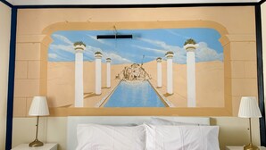 Un dormitori amb un llit gran, dues taules de nit, un mural a la paret i una finestra.