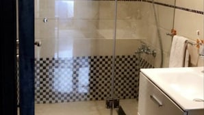 Een moderne badkamer met een douchecabine van glas, een betegeld spatwandje en een wastafelmeubel met spiegel.