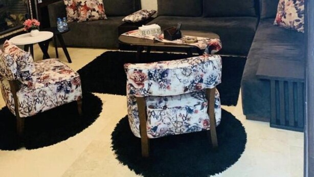 Een moderne woonkamer met een donkere bank, fauteuils met bloemenprint, een salontafel en een open haard.