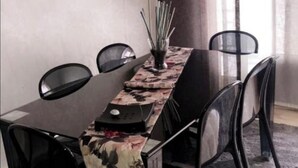 Een eethoek met een lange tafel, vier stoelen, een lamp en een vaas met rieten stengels.
