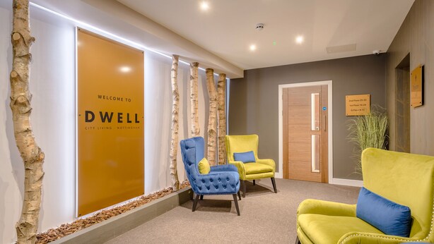 Een receptiegedeelte met een bordje 'Welcome to Dwell City Living - Nottingham', twee fauteuils, een plant en een deur met vloerindicaties.
