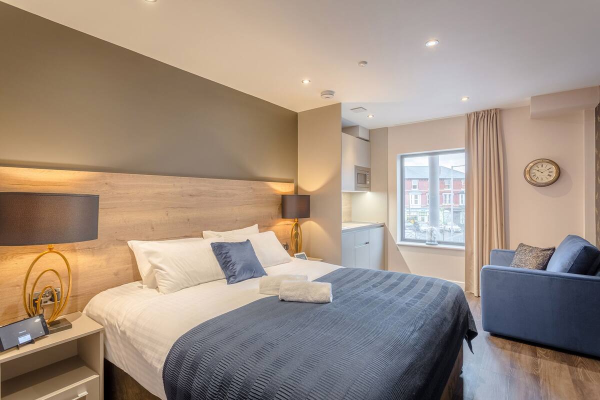 Une chambre d’hôtel moderne dotée d’un grand lit, de tables de chevet, d’un bureau, d’une chaise et offrant une vue sur l’extérieur.