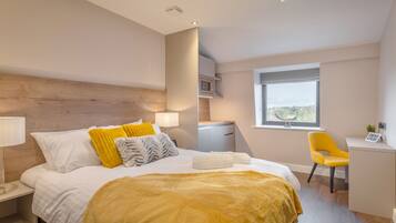 A modern hotel room with a large bed, a desk, and a view of the city.