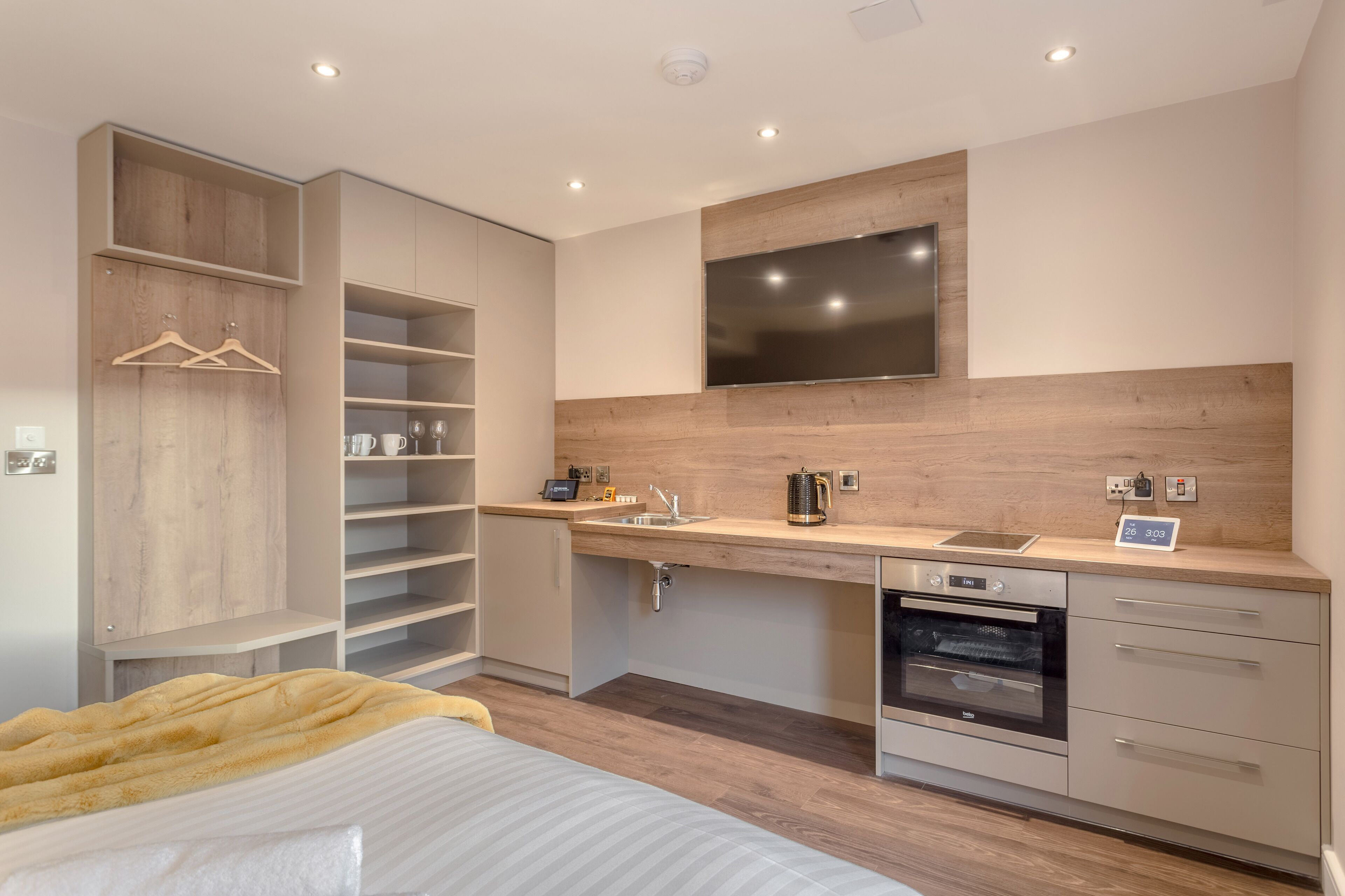 A modern kitchen with a built-in oven, a sink, and a flat-screen TV mounted above the countertop.