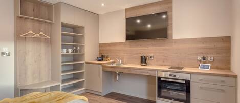 A modern kitchen with a built-in oven, a sink, and a flat-screen TV mounted above the countertop.