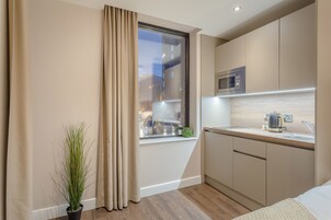 A modern kitchen with a built-in microwave, a kettle, and a window with curtains.