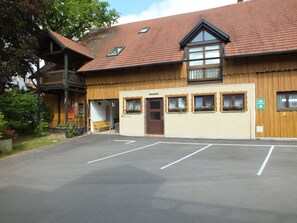 A building with a wooden facade, a balcony, and a parking lot. - Appartements & Reitschule Fuchsenhof (Neunburg vorm Wald)