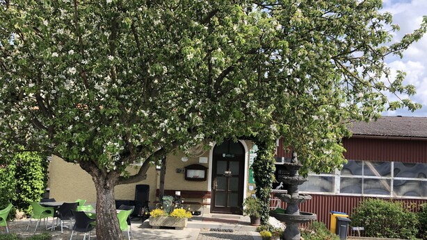 Ein Gebäude mit grüner Tür, einem Steinkunstbrunnen und Außenbestuhlung.