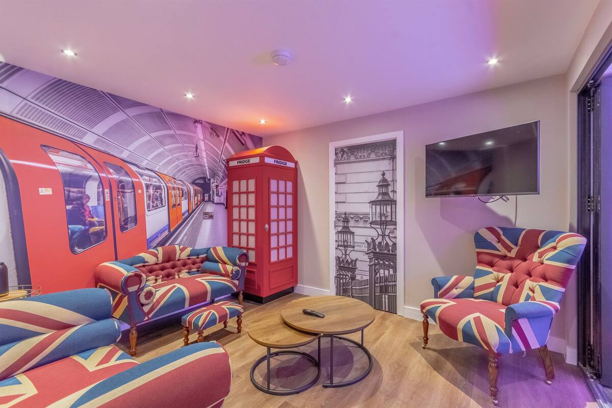 A room with a red telephone booth, a sofa set, a round table, and a wall-mounted TV.