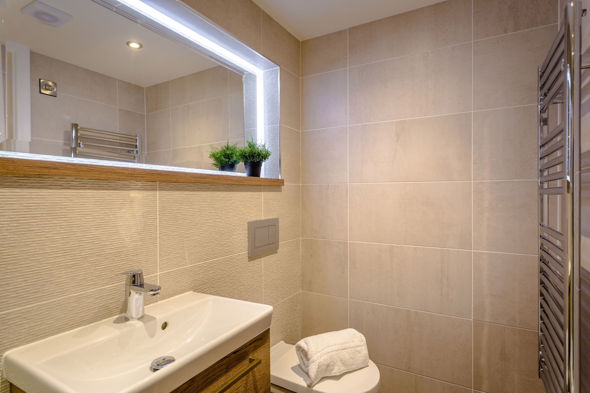 A modern bathroom with a large mirror, a sink, a toilet, and a towel on the toilet.