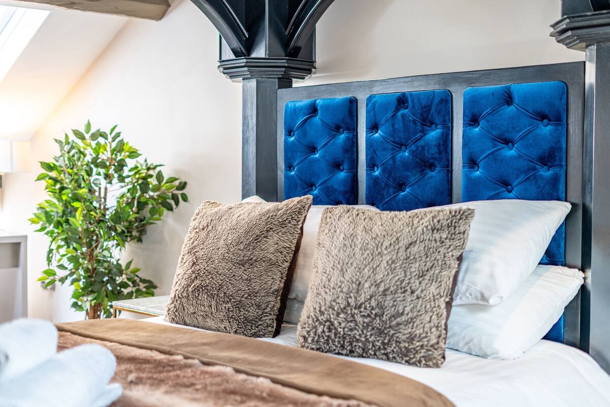 A bedroom with a tufted headboard, plush pillows, and a plant.
