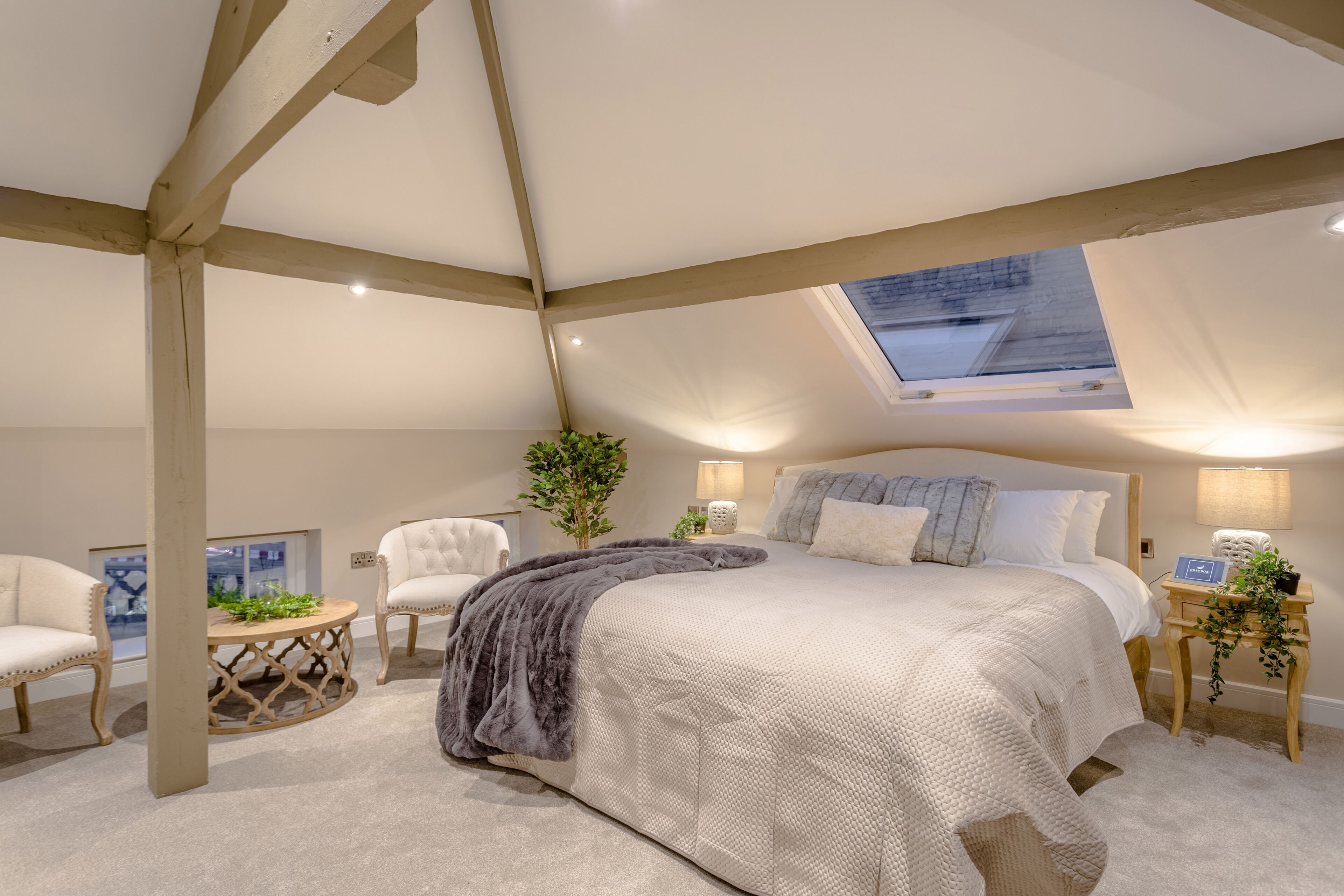 Une chambre spacieuse avec un grand lit, une lucarne, une table ronde en bois et deux chaises.