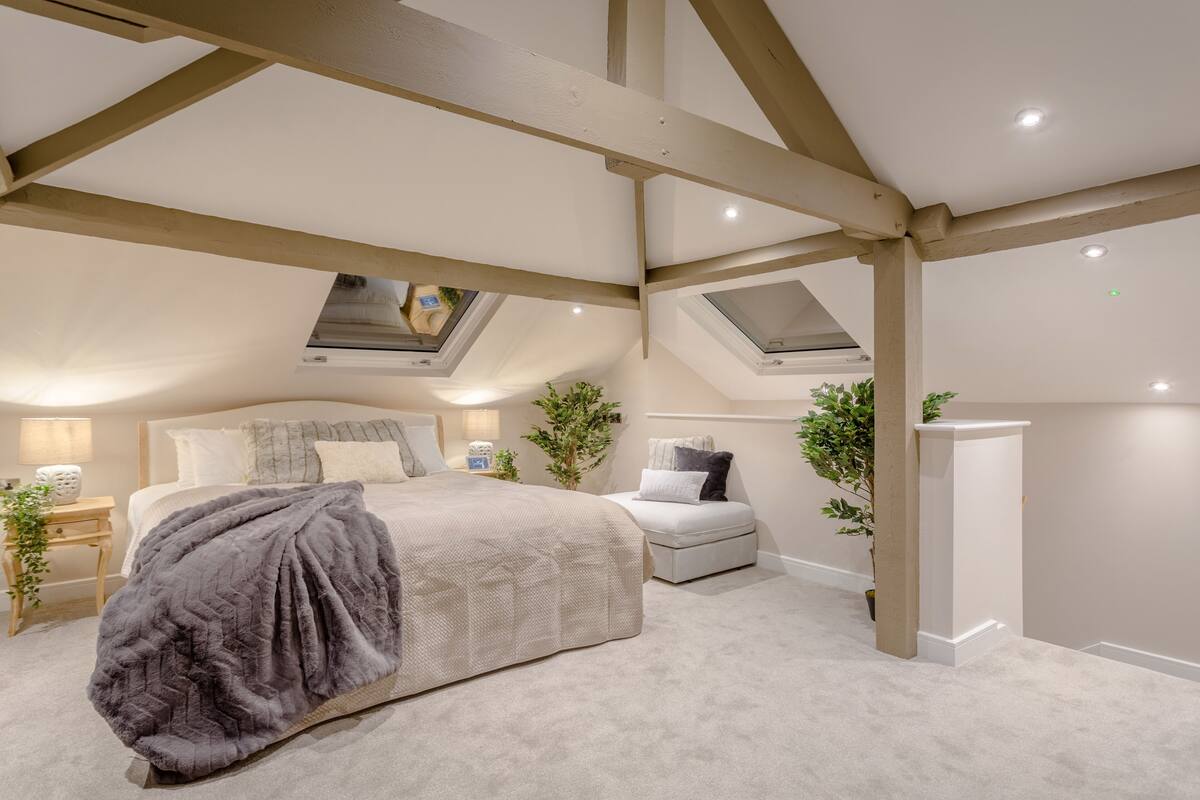 A bedroom with a large bed, a bedside table, a nightstand, a chair, and a skylight.
