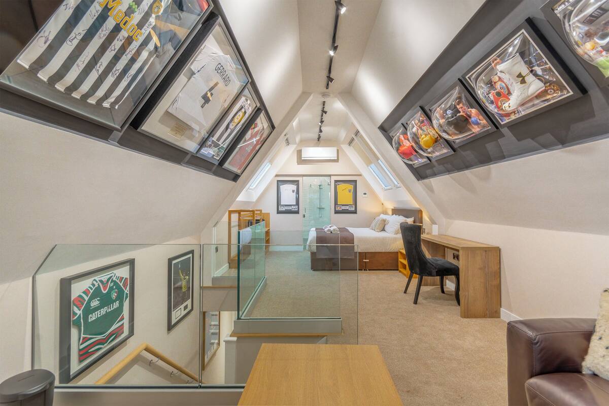 A loft bedroom with a glass ceiling, a bed, a desk, and framed memorabilia on the walls.