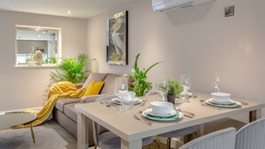 Un comedor con una mesa preparada para cuatro personas, un sofá con una manta amarilla y una planta en maceta.