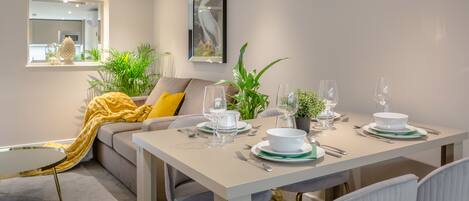 Un coin repas avec une table dressée pour quatre personnes, un canapé recouvert d’un plaid jaune et une plante en pot.
