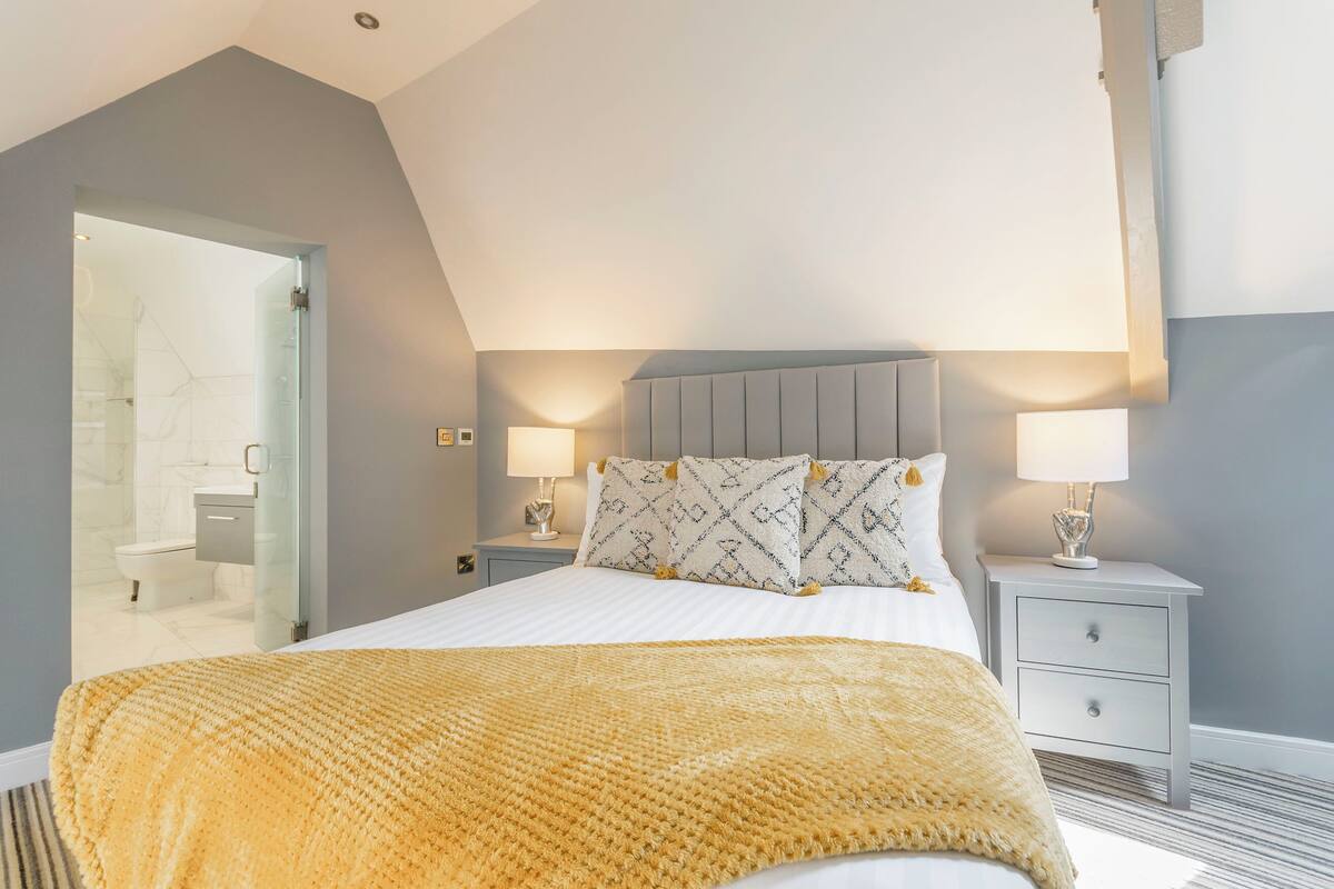 A bedroom with a bed, bedside tables, and a bathroom visible through an open door.