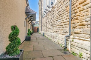 A narrow stone pathway flanked by buildings, with a small tree planter and a metal pipe running along the right wall.