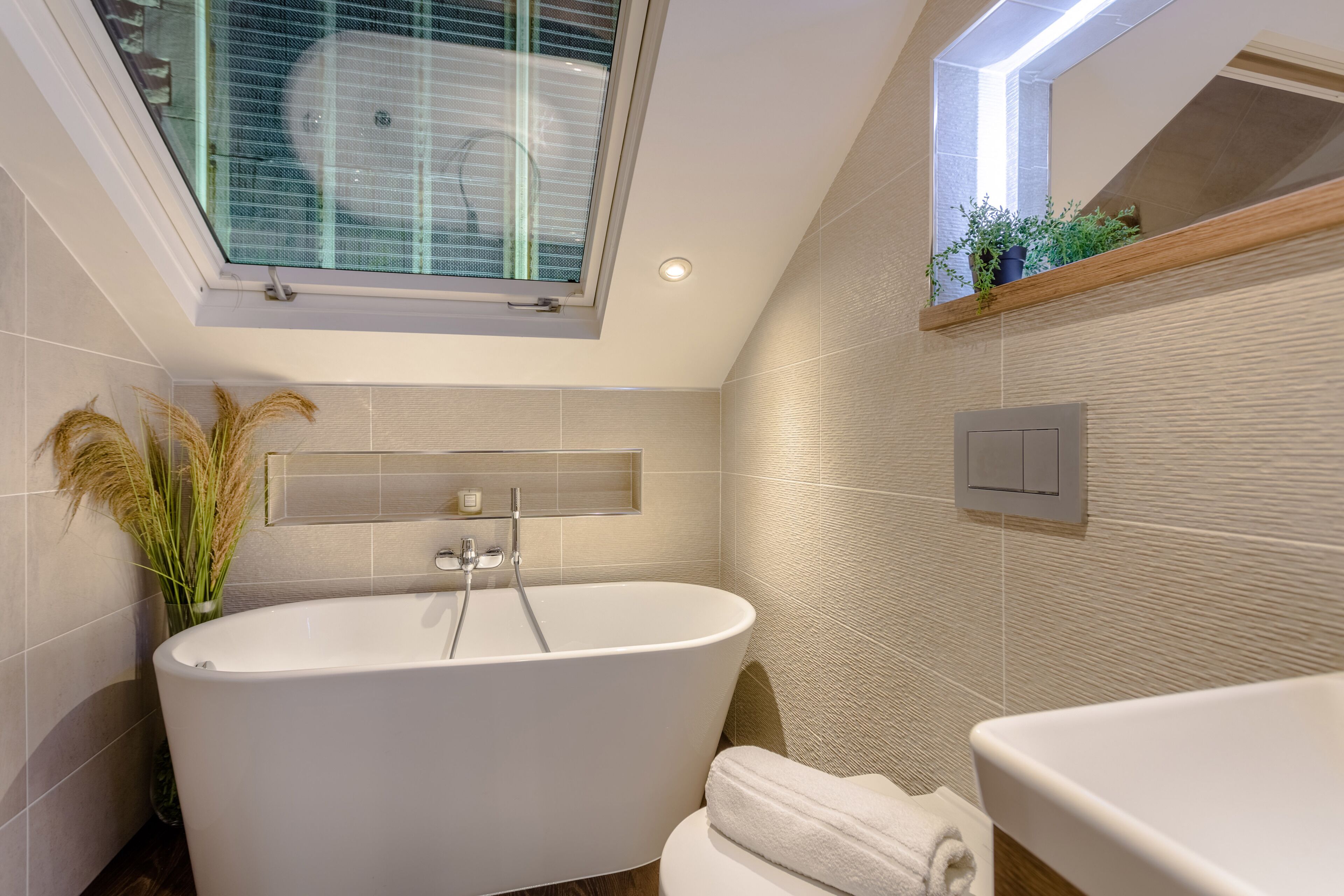 Un baño moderno con una bañera independiente, una ventana con vistas y un estante de madera con plantas.