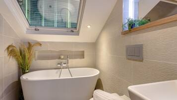 Un baño moderno con una bañera independiente, una ventana con vistas y un estante de madera con plantas.