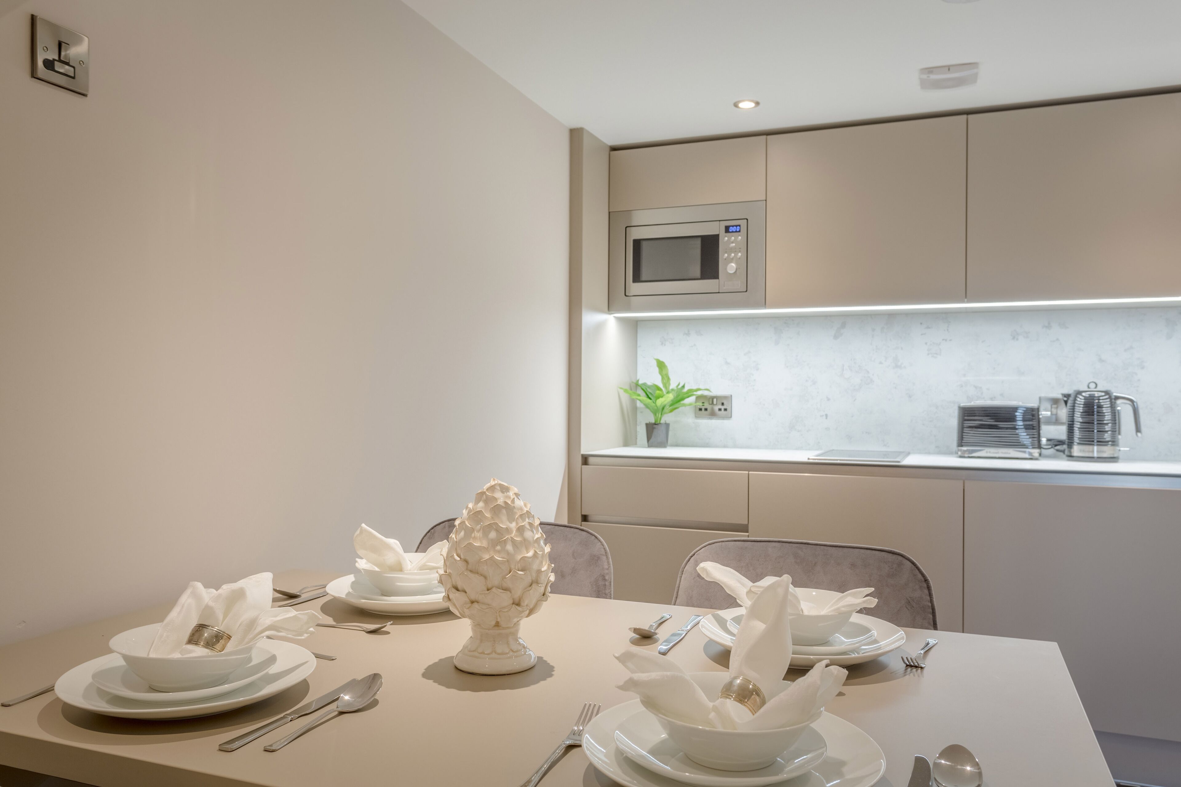A modern dining area with a table set for four, a microwave above, and a plant on the counter.