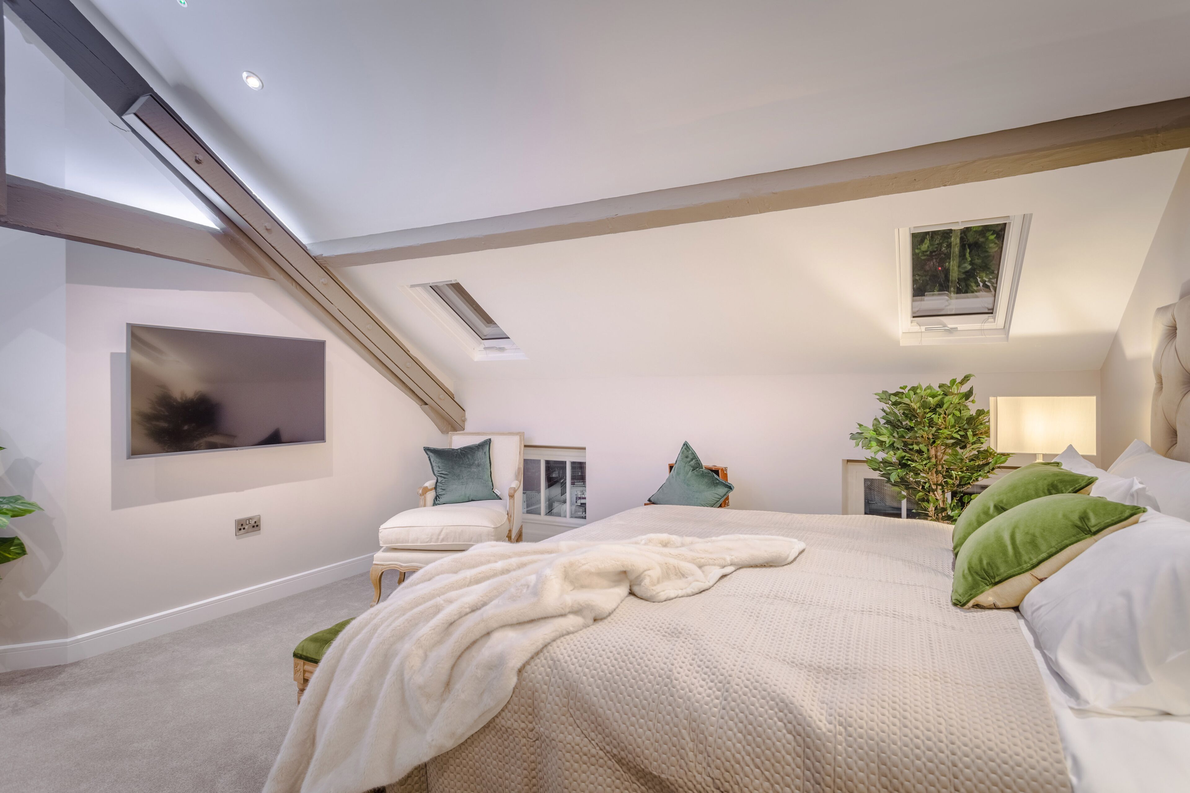 Ein Schlafzimmer mit einem großen Bett, einem Sessel, einem kleinen Tisch, einer Pflanze und einem Fenster.