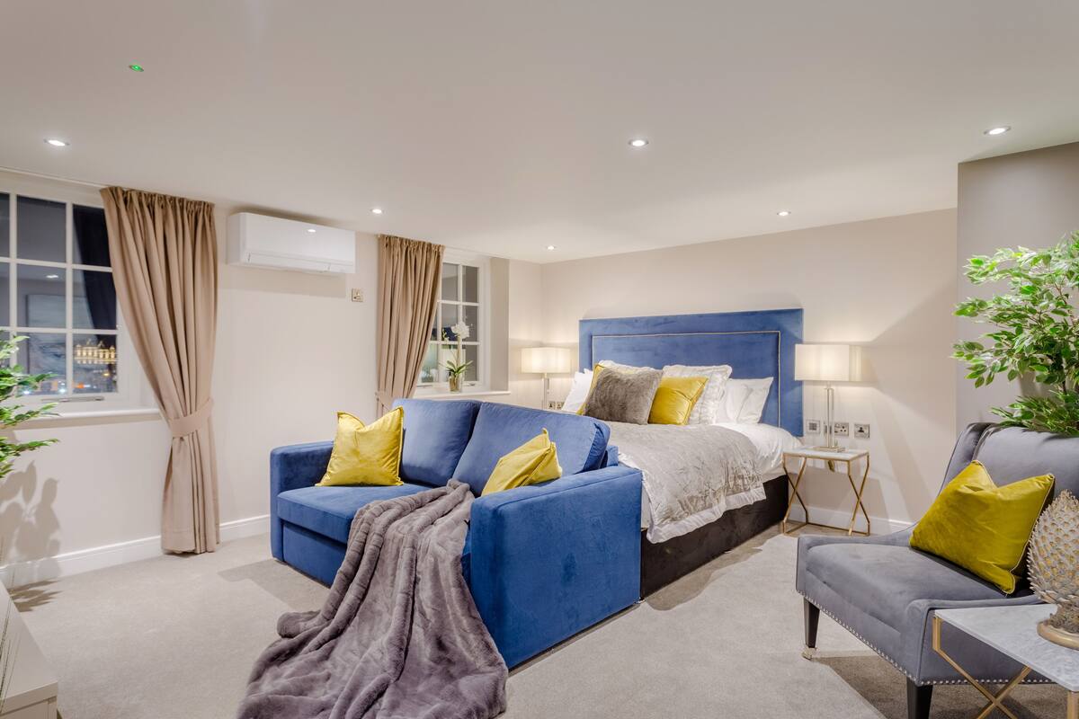 A modern hotel room with a large bed, a blue sofa, and a grey armchair.