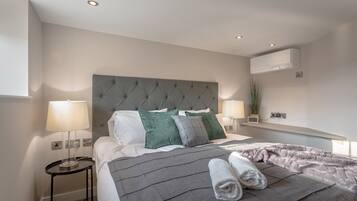 A modern hotel room with a large bed, two bedside tables, a grey headboard, and an air conditioning unit on the wall.