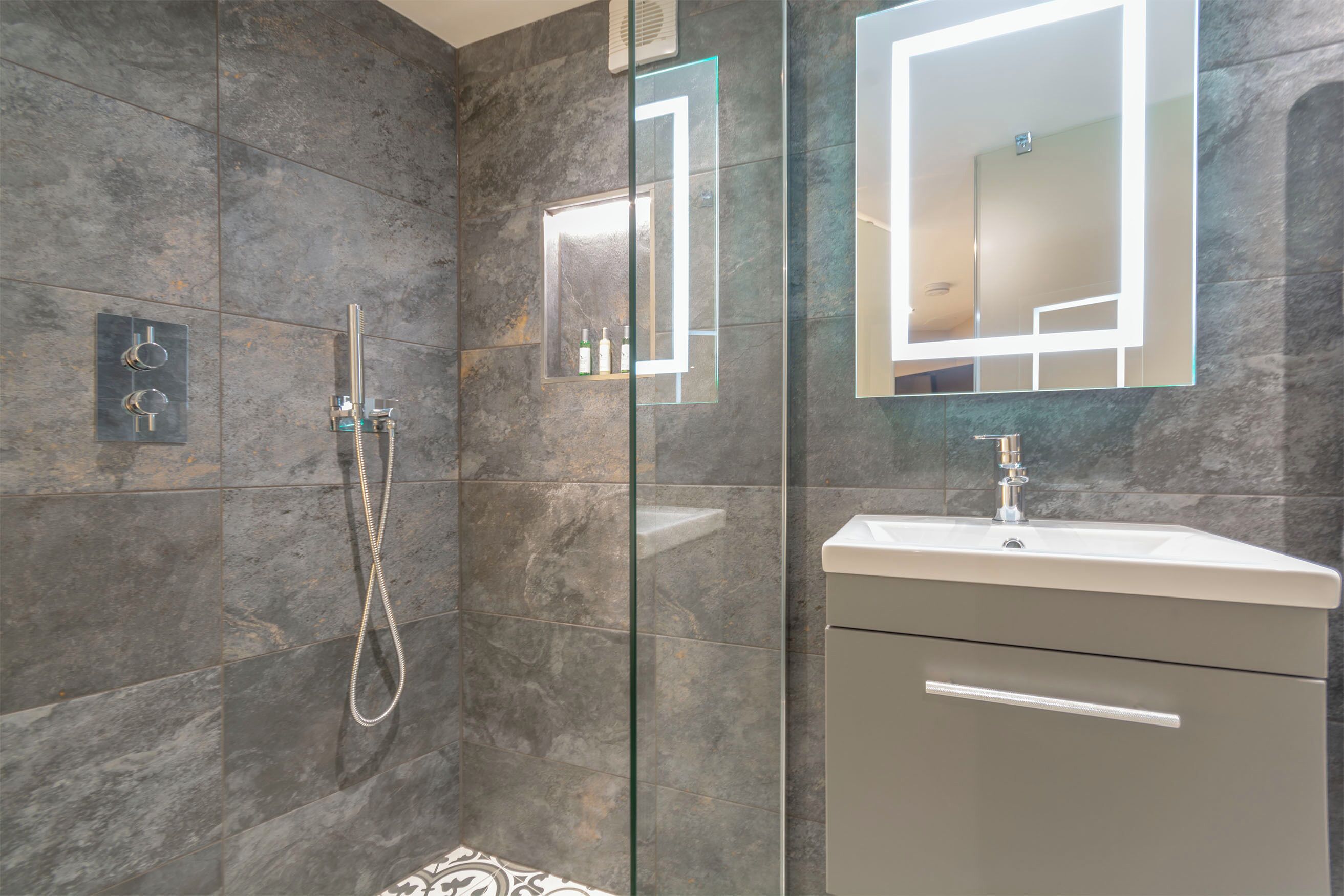 A modern bathroom with a glass-enclosed shower, a vanity with a mirror, and a built-in shelf with toiletries.
