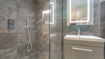 A modern bathroom with a glass-enclosed shower, a vanity with a mirror, and a built-in shelf with toiletries.