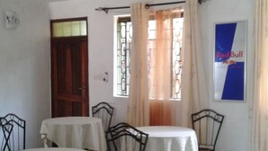 A dining area with two tables, chairs, a ceiling fan, and a window with curtains. - Greenview Guest House (Kisumu)