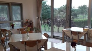 A dining area with tables and chairs, large windows with curtains, and a view of greenery outside. - Maple Farm (Guangfu)