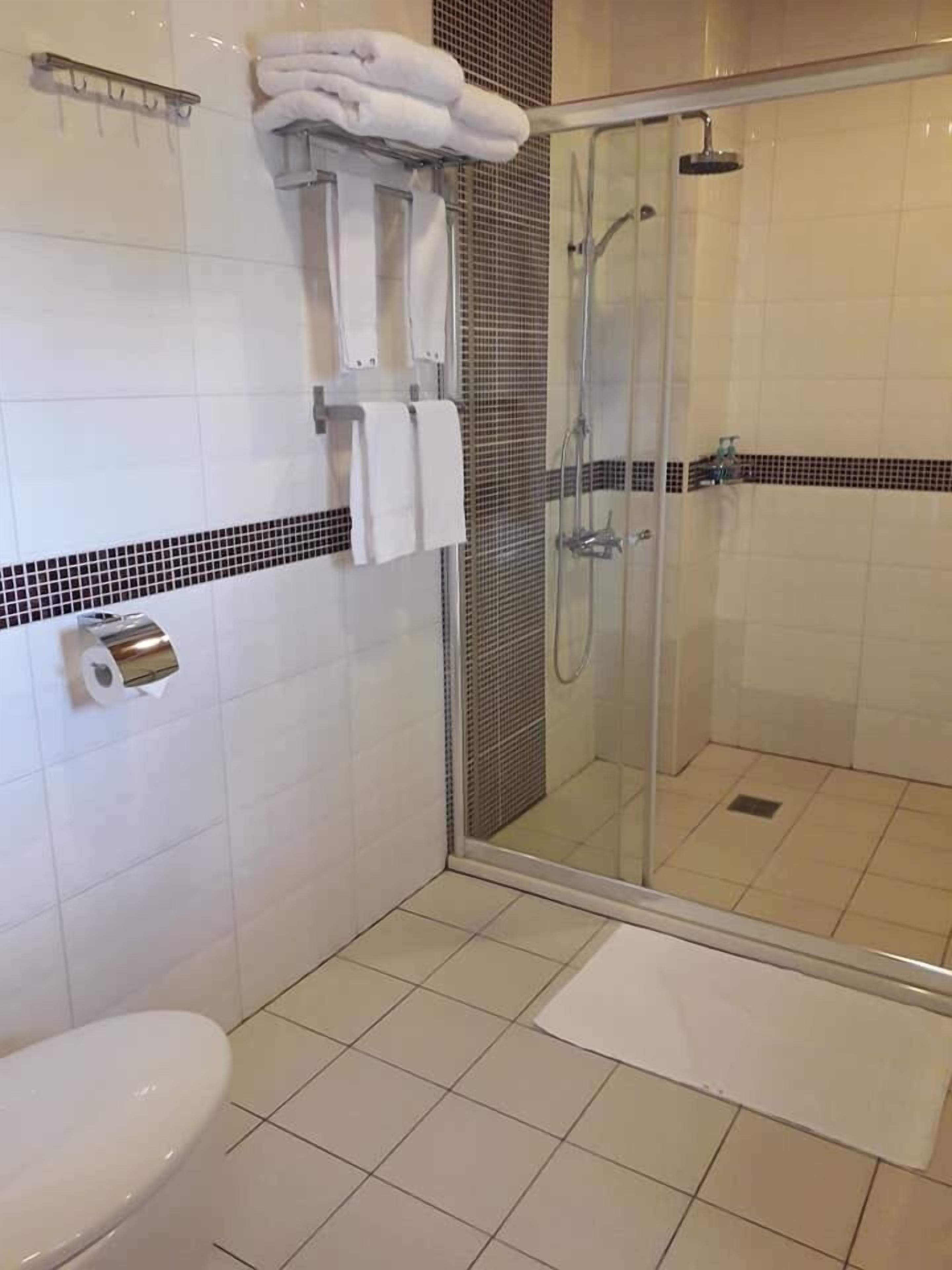 A bathroom with a toilet, a glass-enclosed shower, and a towel rack with folded towels.