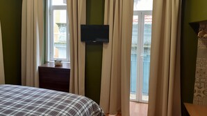 Une chambre à coucher avec un lit, un téléviseur fixé au mur et une fenêtre avec des rideaux.