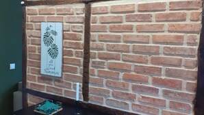 Un mur de briques orné d’une horloge et d’une œuvre d’art encadrée. Devant le mur, on trouve une petite table avec des tabourets.