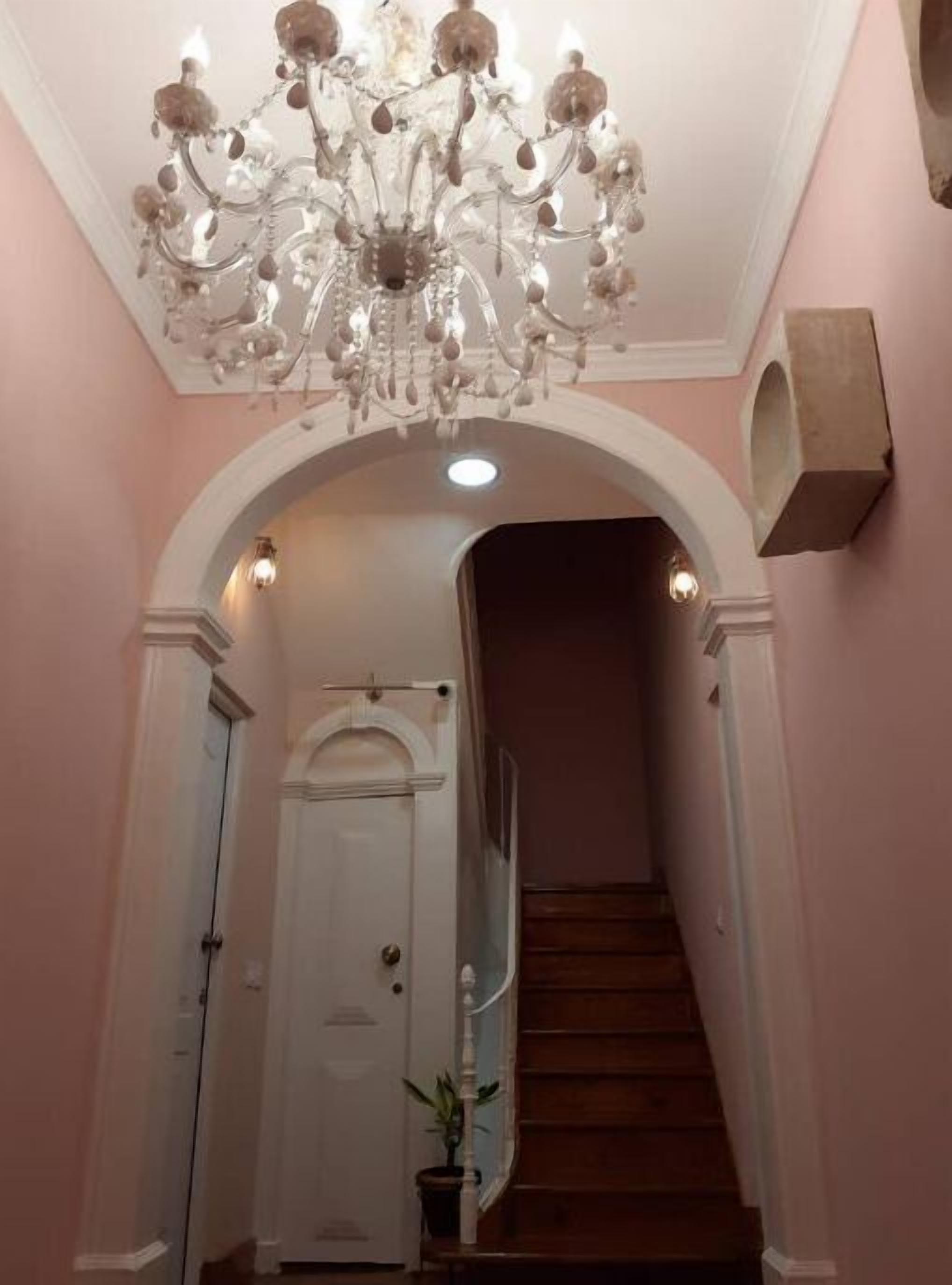 Una escalera con una puerta blanca al final, un candelabro encima y una planta en maceta abajo.