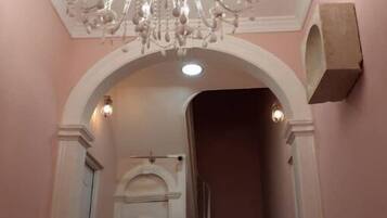Una escalera con una puerta blanca al final, un candelabro encima y una planta en maceta abajo.