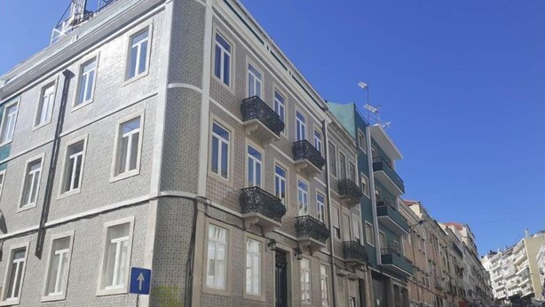 Un immeuble à plusieurs étages, doté d’une façade ornée, de balcons et d’un espace de stationnement où sont garées des voitures.