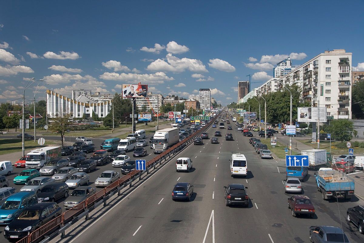A multi-lane highway with moderate traffic, surrounded by urban buildings and billboards.