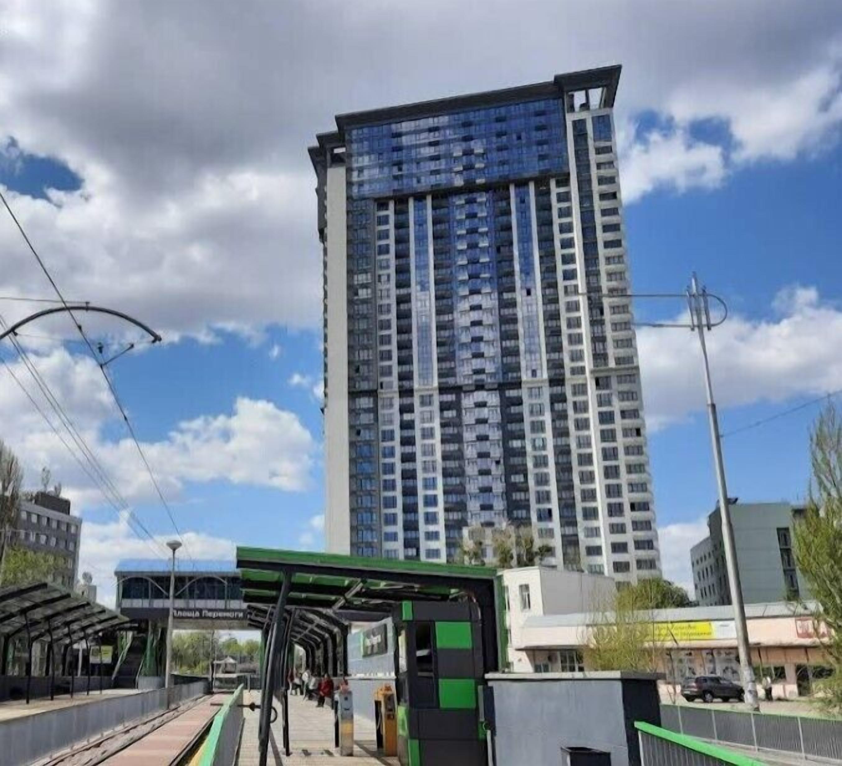 A high-rise building with a modern design, a covered pedestrian walkway, and a train station platform.