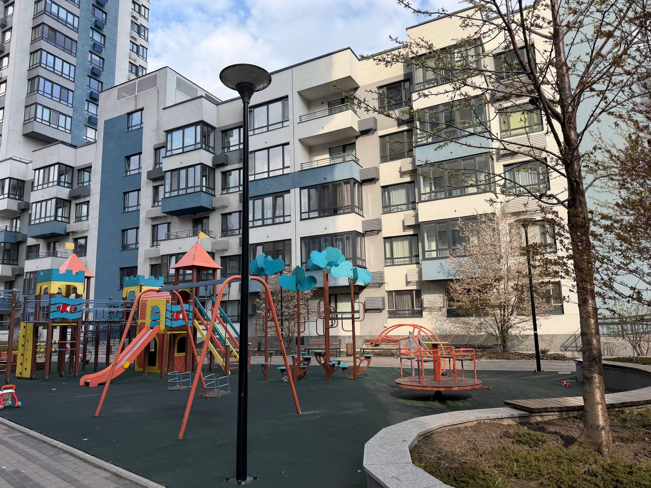 A playground with swings and slides, surrounded by apartment buildings.