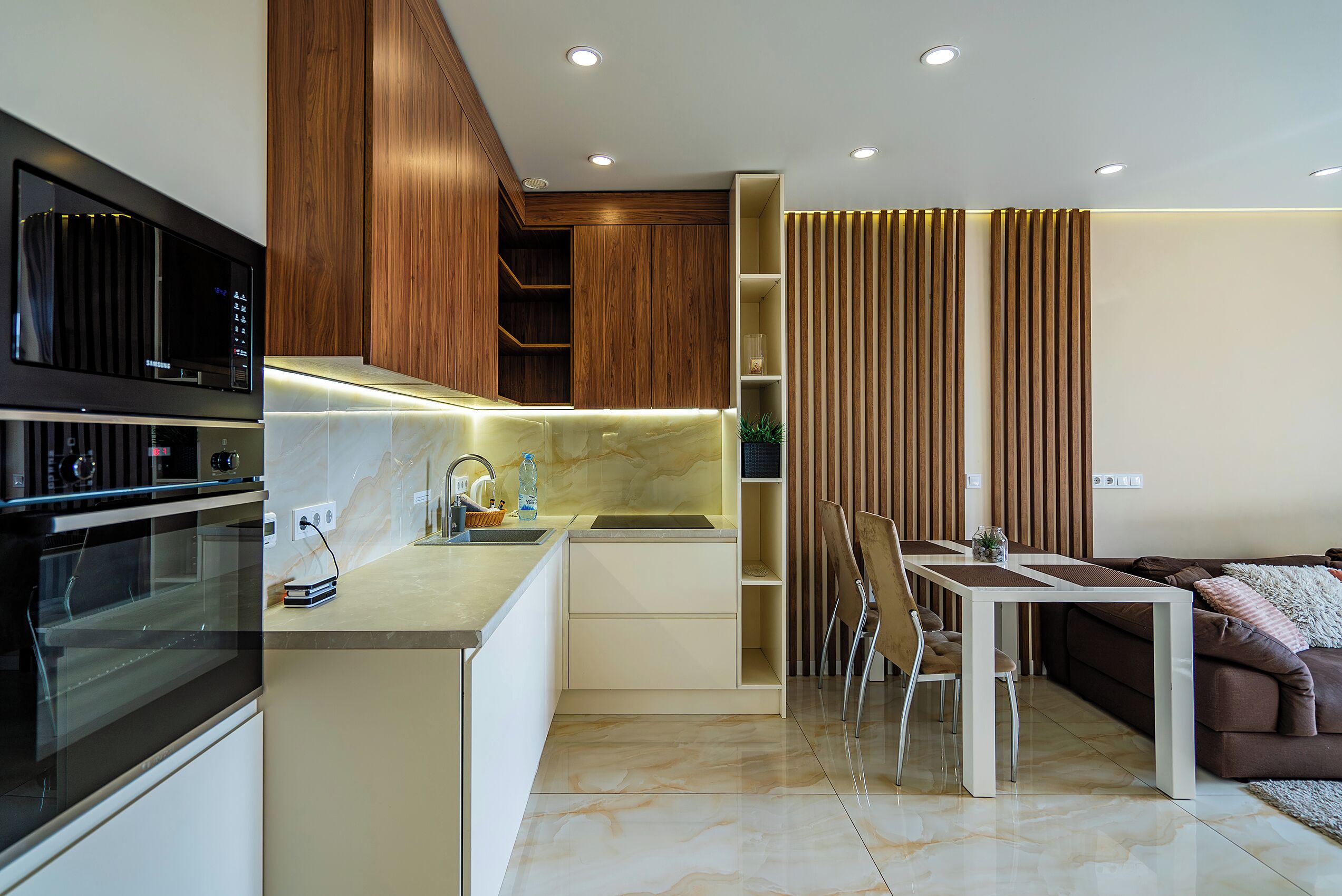 Una cocina moderna con horno empotrado, una zona de comedor con mesa y sillas, y una pared decorativa de madera.