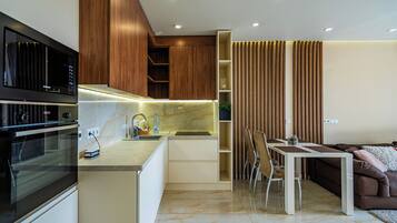 Una cocina moderna con horno empotrado, una zona de comedor con mesa y sillas, y una pared decorativa de madera.