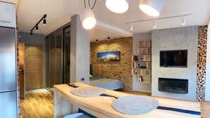 Une cuisine moderne avec un plan de travail en bois, deux tabourets de bar, un mur en briques, une cheminée et un téléviseur fixé au mur.