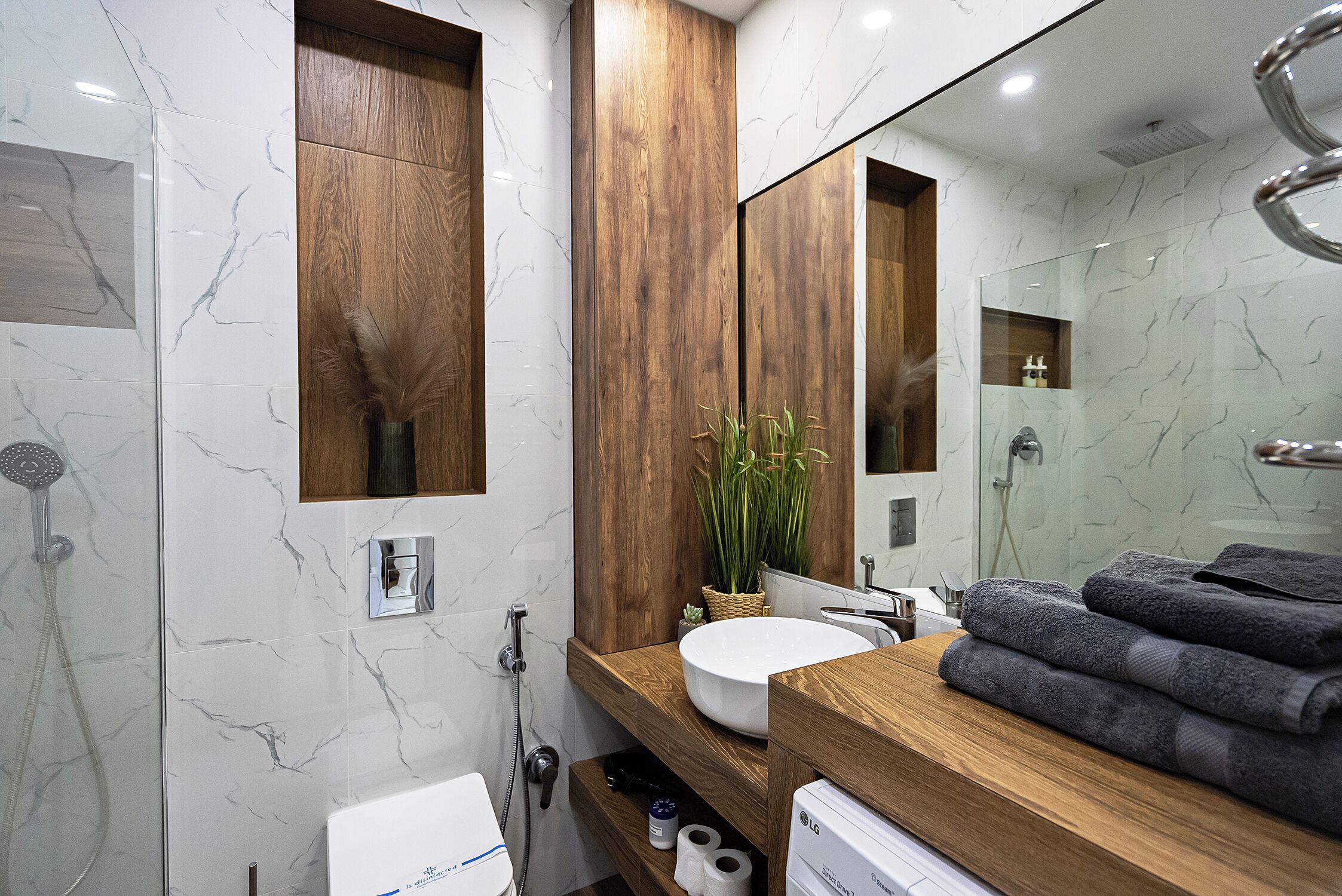 A modern bathroom with a wooden vanity, a large mirror, a white sink, and a shower area.