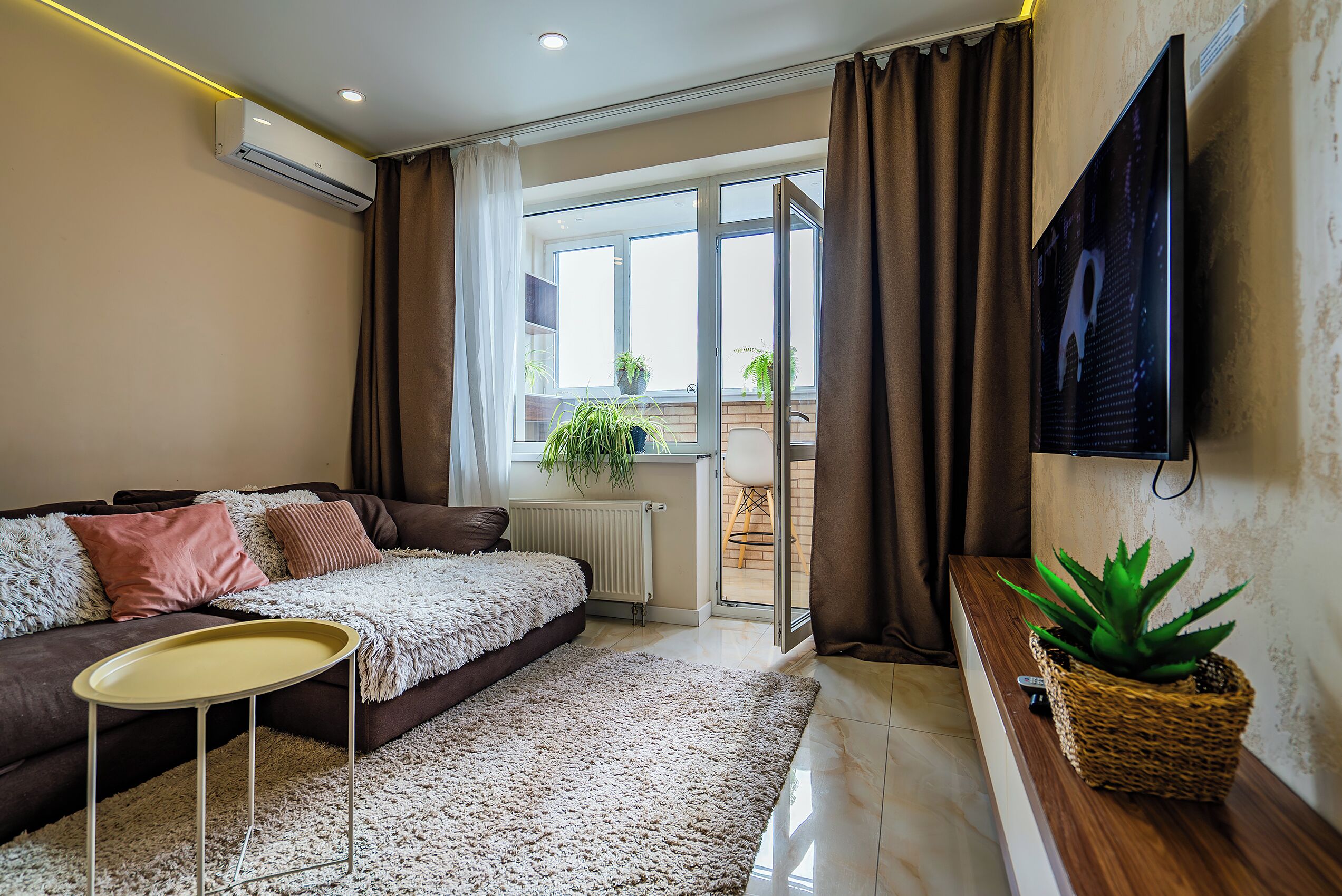 A modern living room with a sofa, a small table, a potted plant, and a TV mounted on the wall.