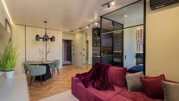 Una sala de estar moderna con un sofá rojo, una zona de comedor con mesa y sillas, y un espejo grande que refleja la habitación.