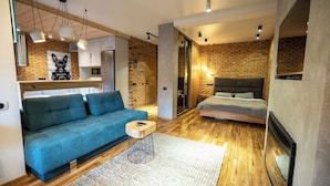 Un salon moderne avec un canapé bleu, une petite table ronde et un lit doté d’une tête de lit grise.