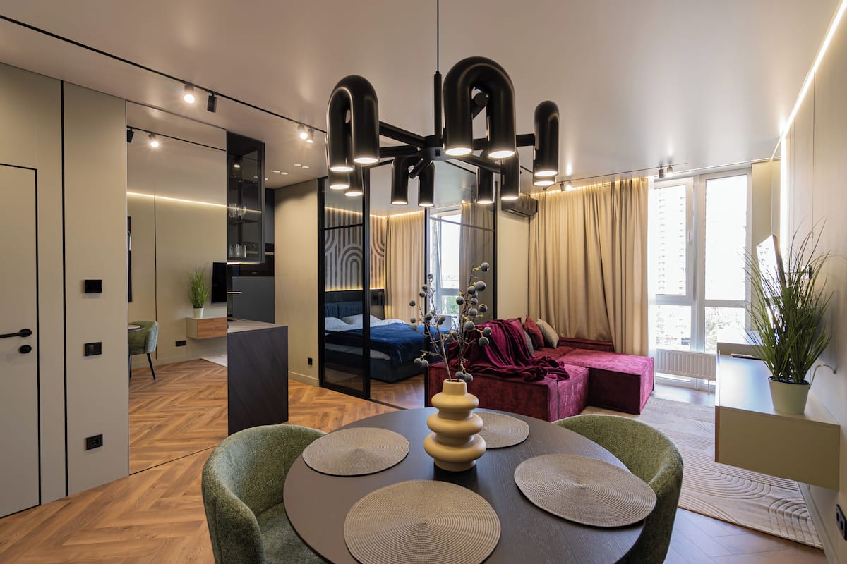 Un interior moderno con zona de comedor, sofá, cama y un ventanal grande.